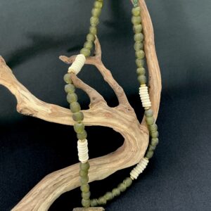 Green trade beaded and bone necklace with carved bone pointed pendant hung on a branch with black background