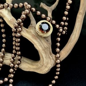 Gold pendant with a brown stone with a strand of bronze pearls on a branch with black background.