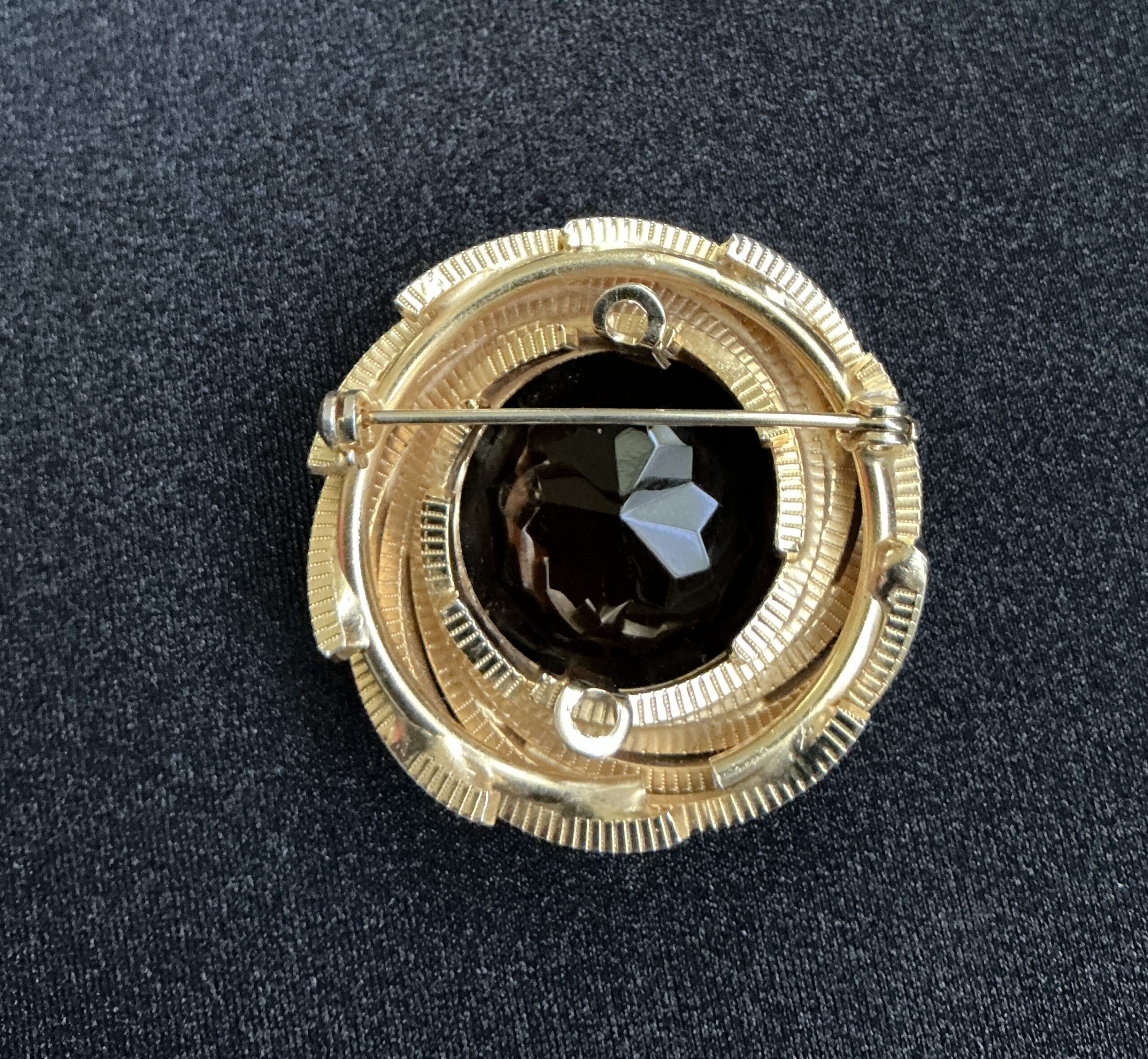 Gold-tone circular brooch with a faceted black stone and pin clasp