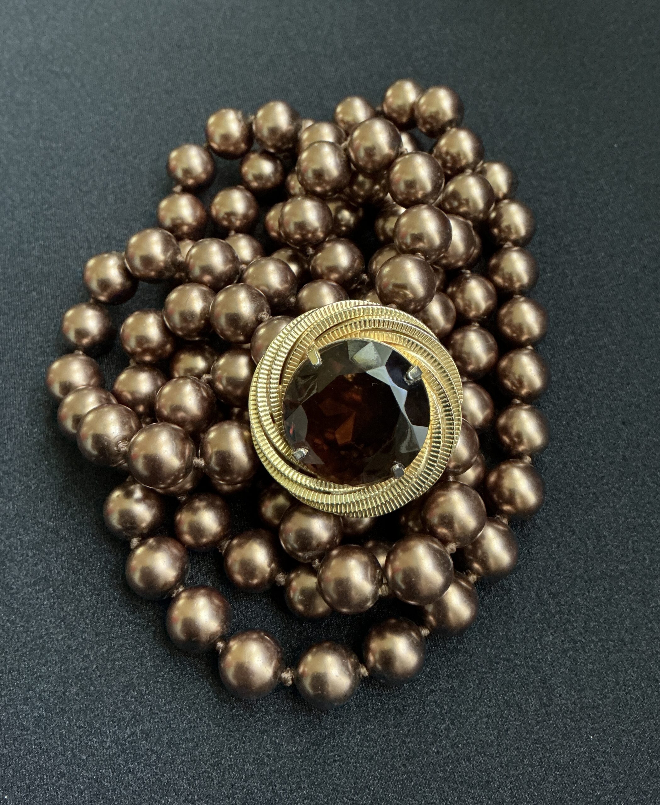 Gold-tone brooch with a large brown gemstone on a strand of bronze pearls