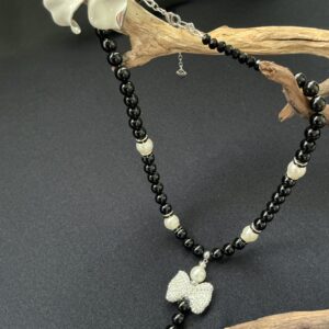 Black beaded necklace with pearl, bow, and heart charms, accented by a white flower brooch.