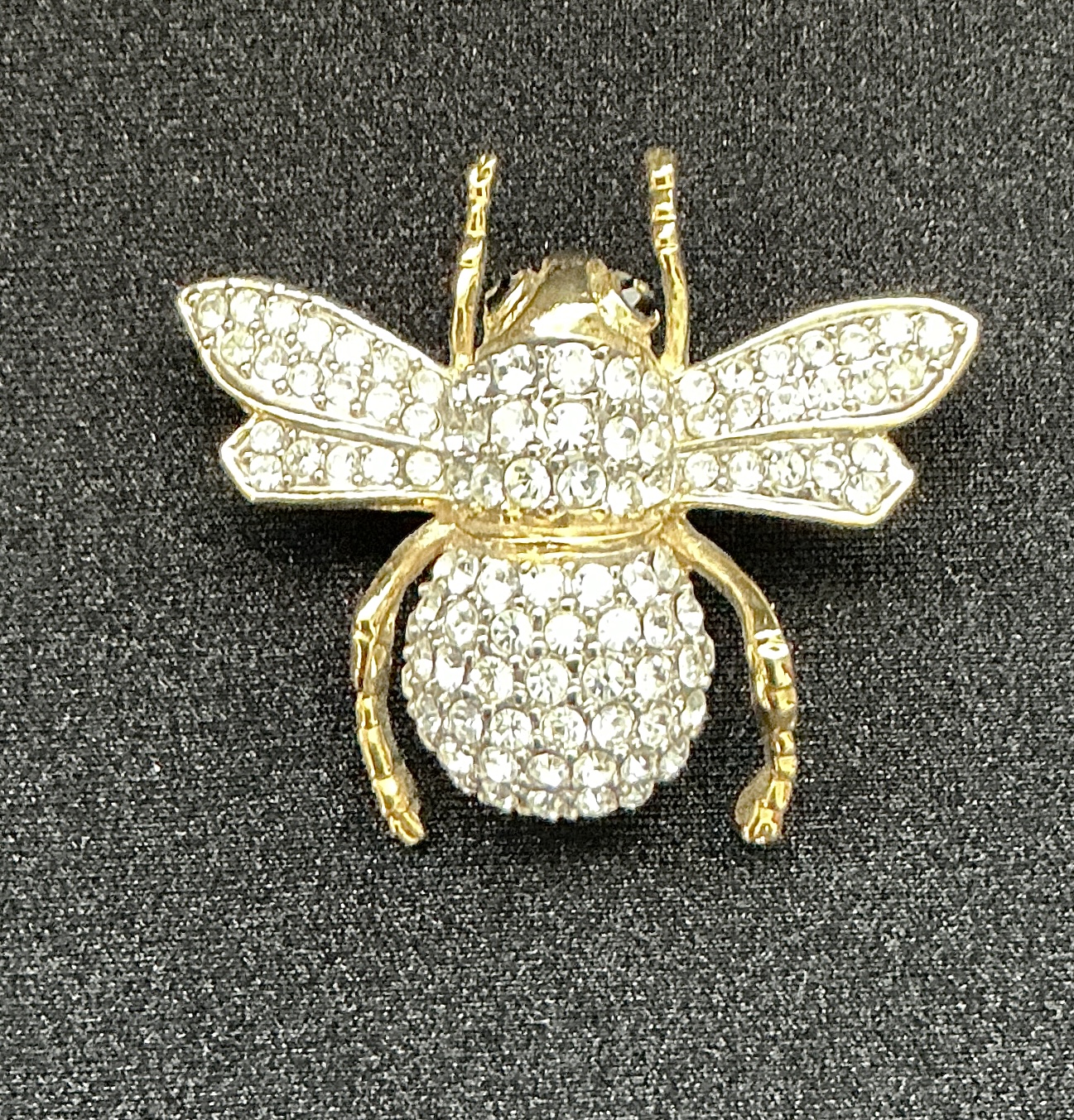 Gold bee brooch encrusted with clear rhinestones on a dark fabric background.
