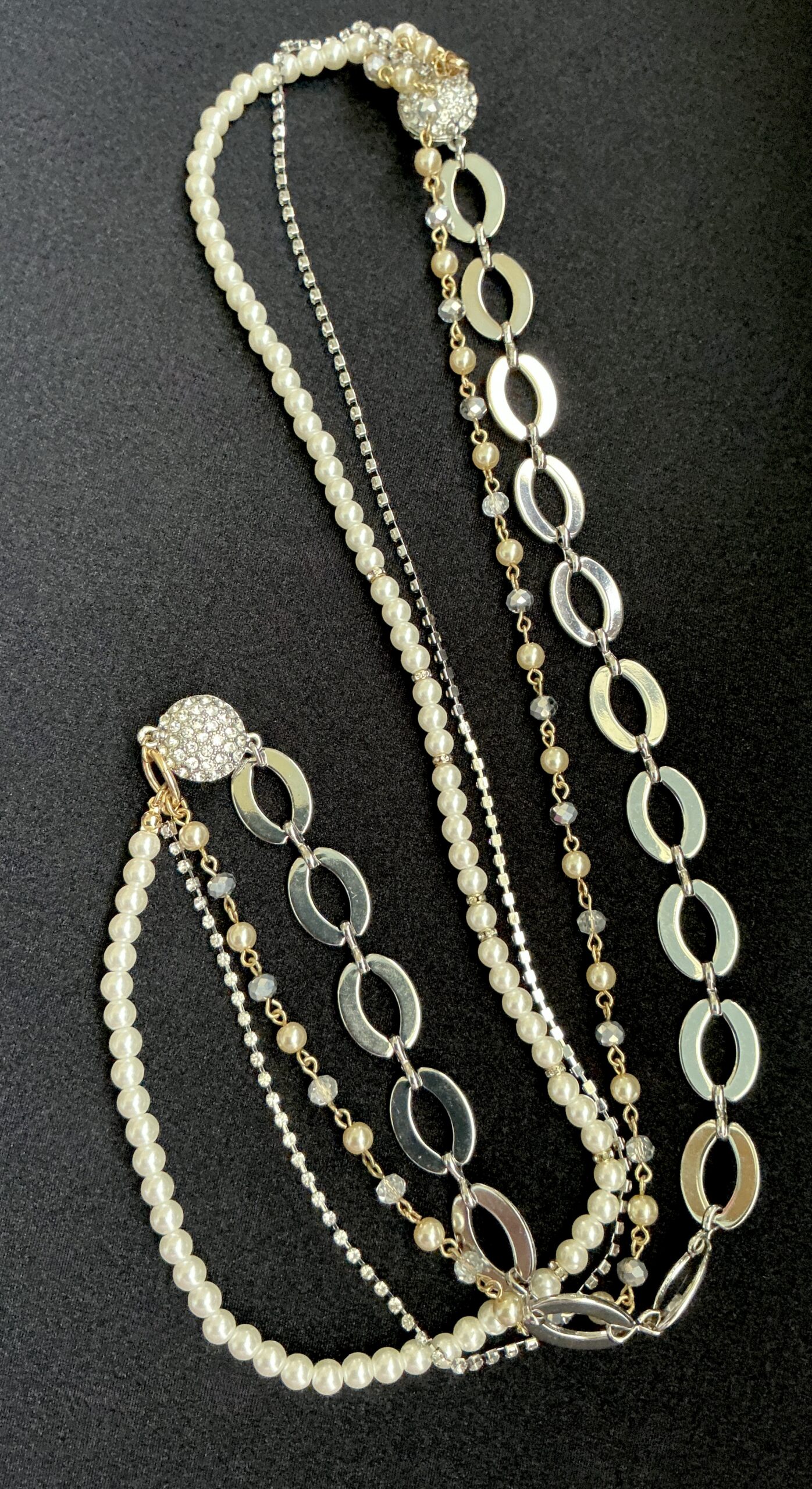 Layered pearl and silver necklaces with crystal accents on black fabric