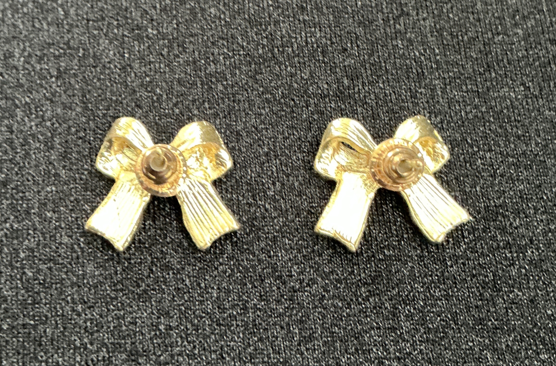 Gold bow earrings with a textured fabric background