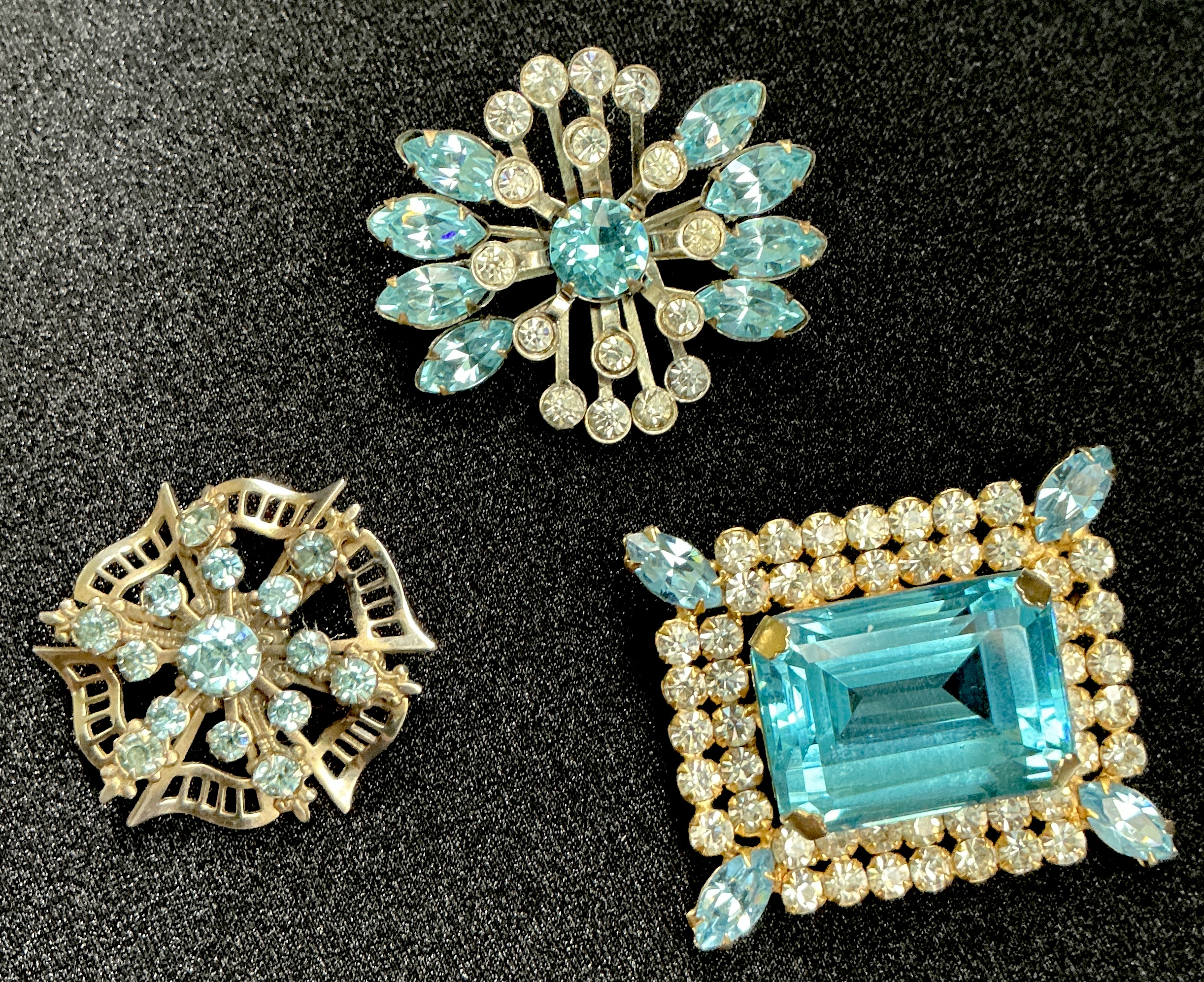 Three vintage turquoise rhinestone brooches: floral, starburst, and rectangular designs.